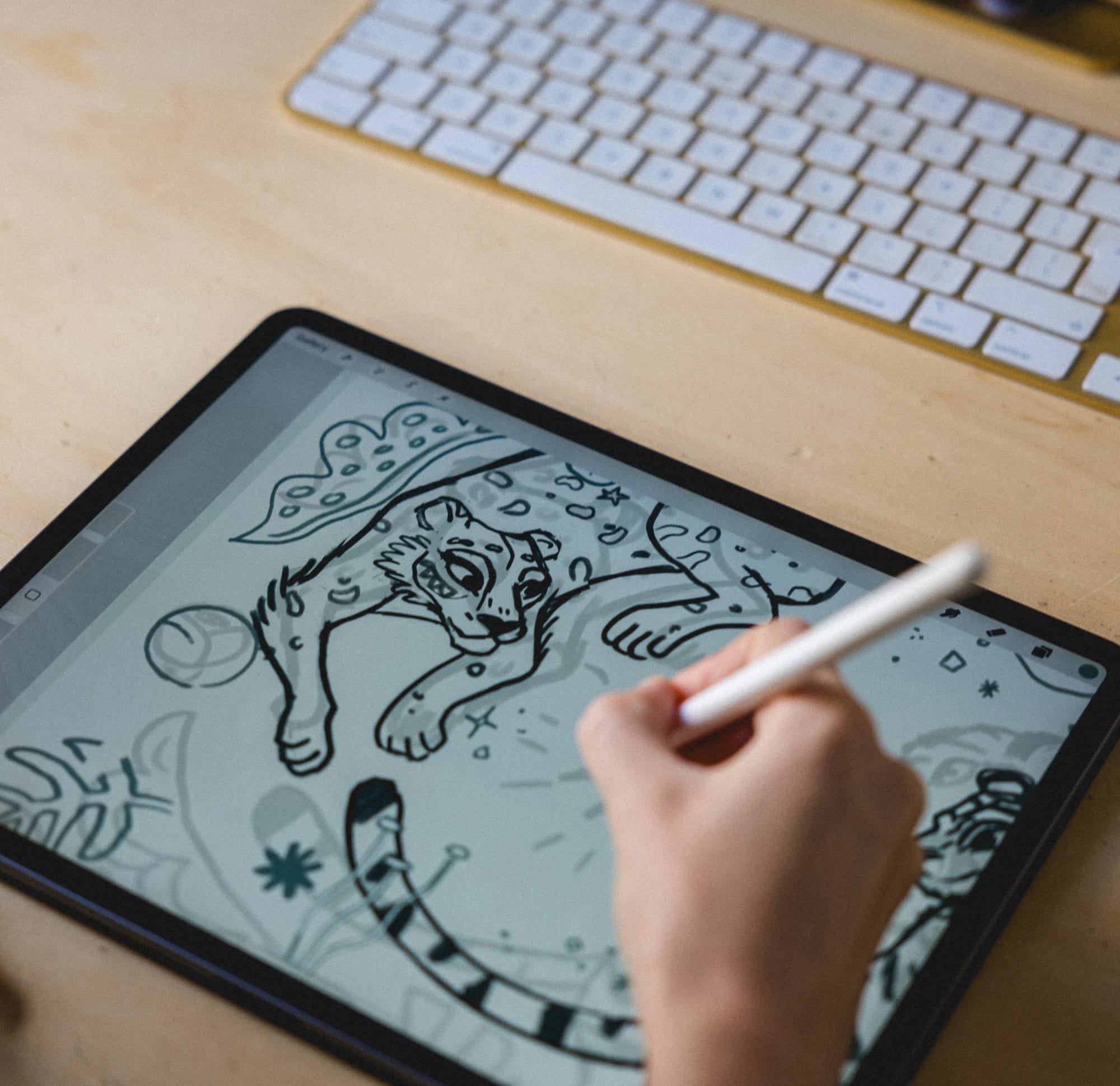 Una persona usando un lápiz óptico para dibujar un león en una tableta digital, con un teclado al fondo.