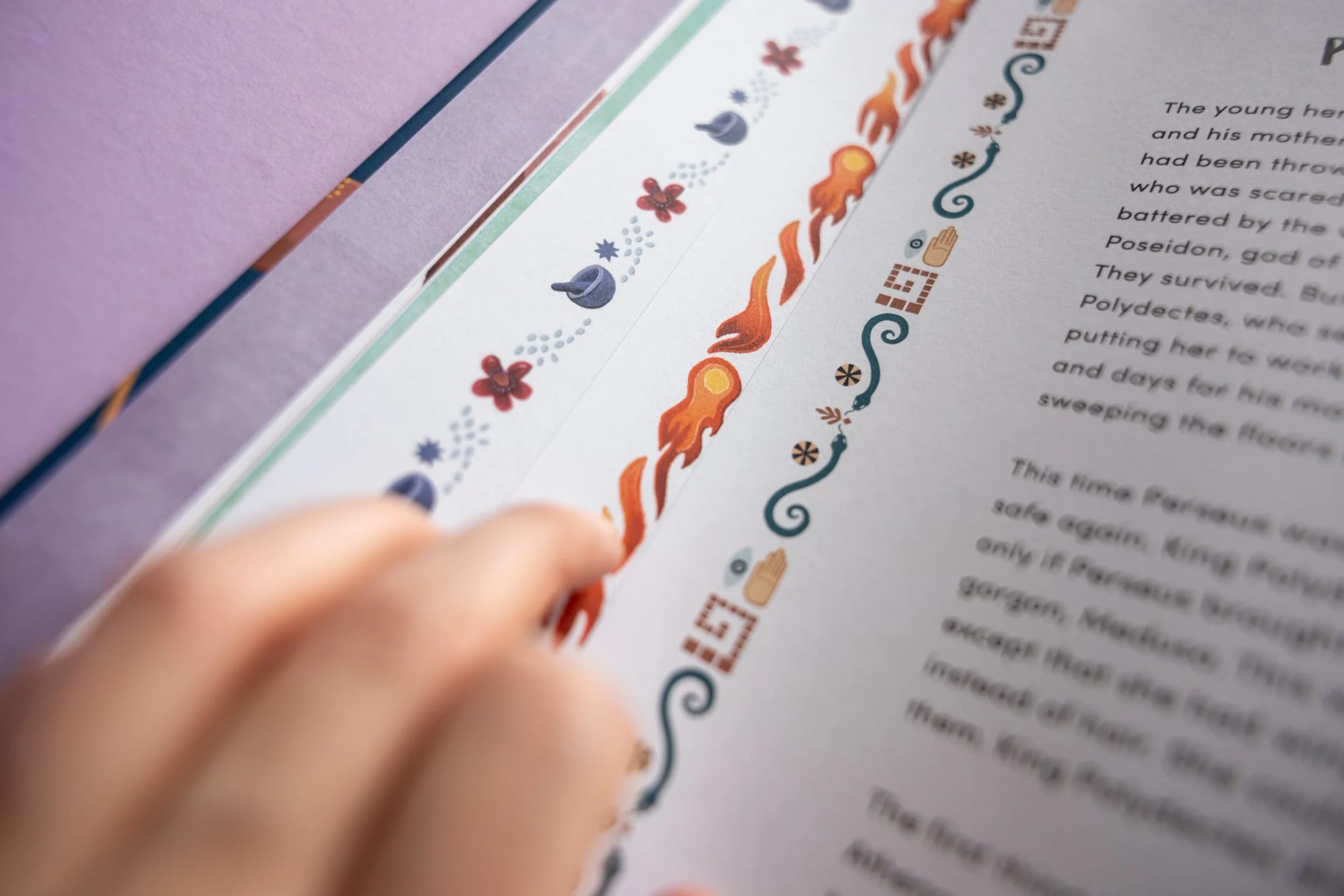 Nahaufnahme einer Hand, die auf eine farbenfrohe dekorative Bordüre auf einer Druckseite zeigt, mit teilweise sichtbarem Text. Die Bordüre zeigt Illustrationen von Blumen, Flammen und abstrakten Formen.