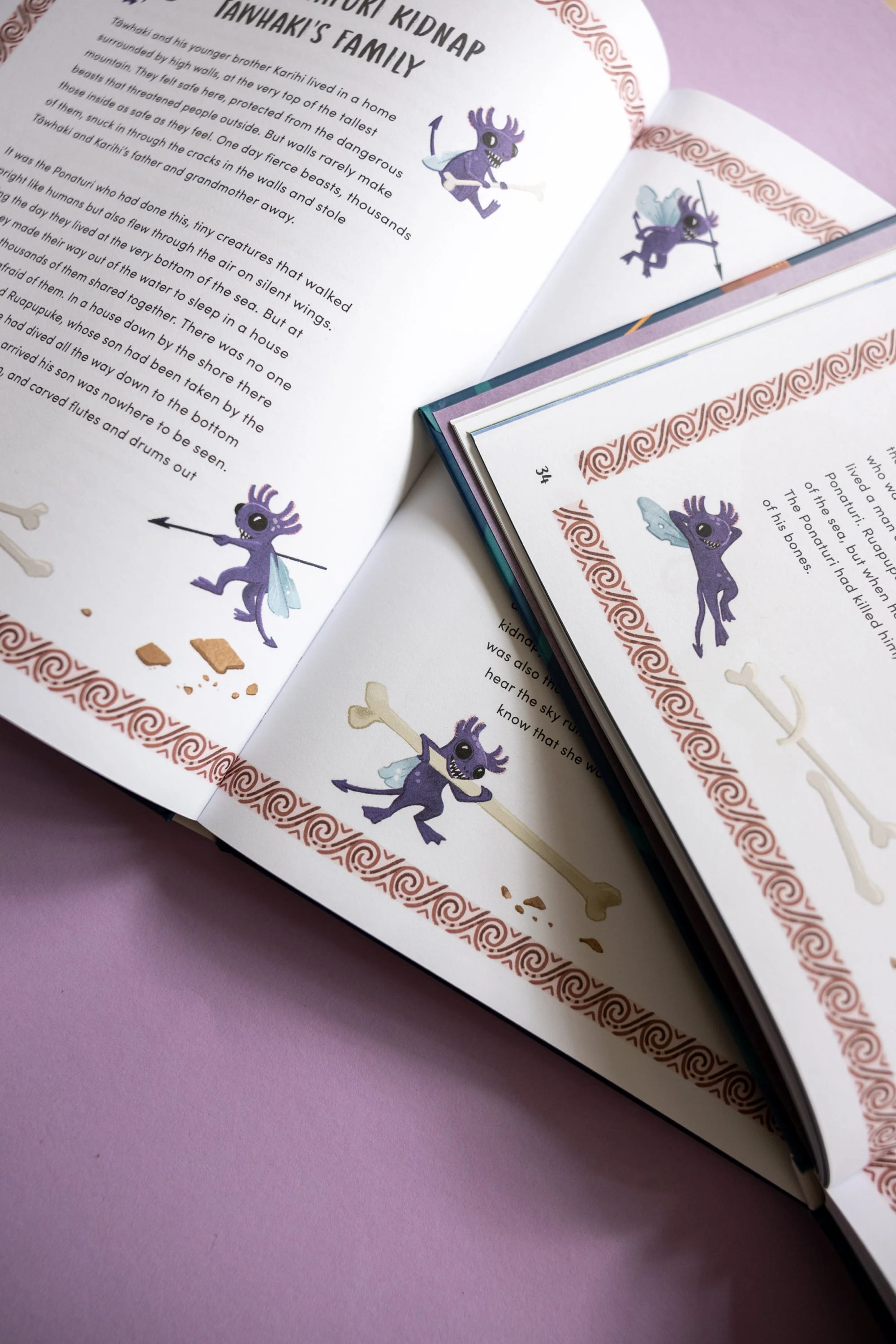 Aufgeschlagenes Buch mit Illustrationen eines violetten feenartigen Wesens mit Flügeln, das einen Speer und einen Knochen hält, mit dekorativer Bordüre und Text zu einer mythologischen Geschichte auf rosa Hintergrund.