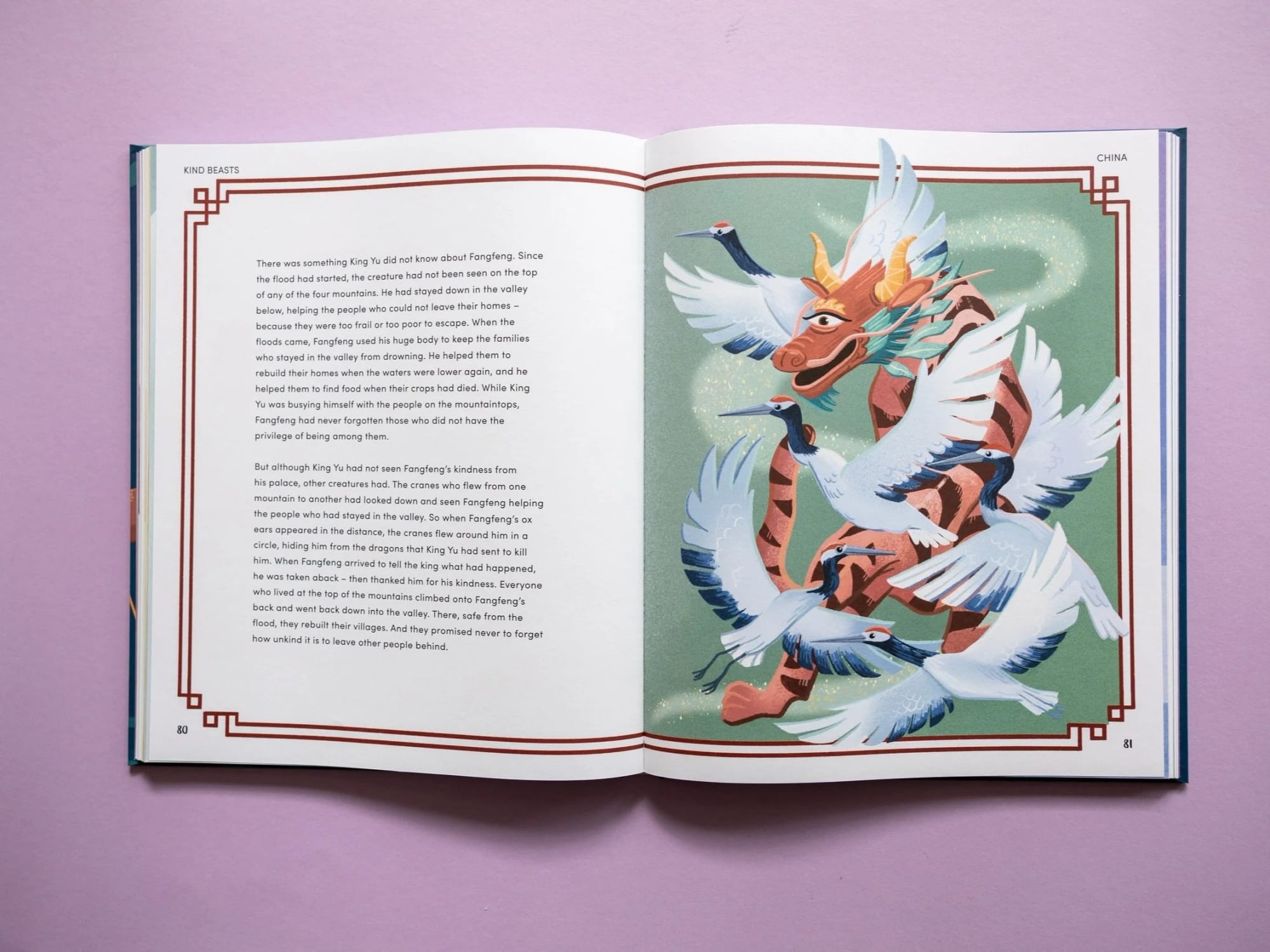 Aufgeschlagenes Buch mit einer farbenfrohen Illustration eines Drachen und mehrerer um ihn herum fliegender Kraniche auf rosa Hintergrund.