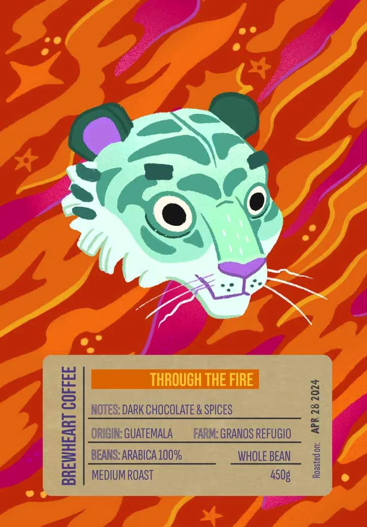Illustration eines Tigerkopfs mit grün-weißem Gesicht, lila Nase und Ohrenspitzen vor einem feurigen orange-rot-violetten Hintergrund, mit einem Kaffeeetikett mit dem Titel ‚Through the Fire‘.