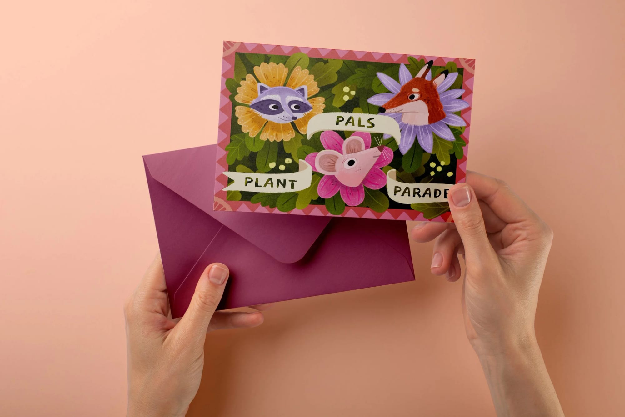 Une personne tient une enveloppe rose et une carte colorée avec des animaux en dessin animé, portant l'inscription « Plant Pals Parade », sur un fond rose pâle.